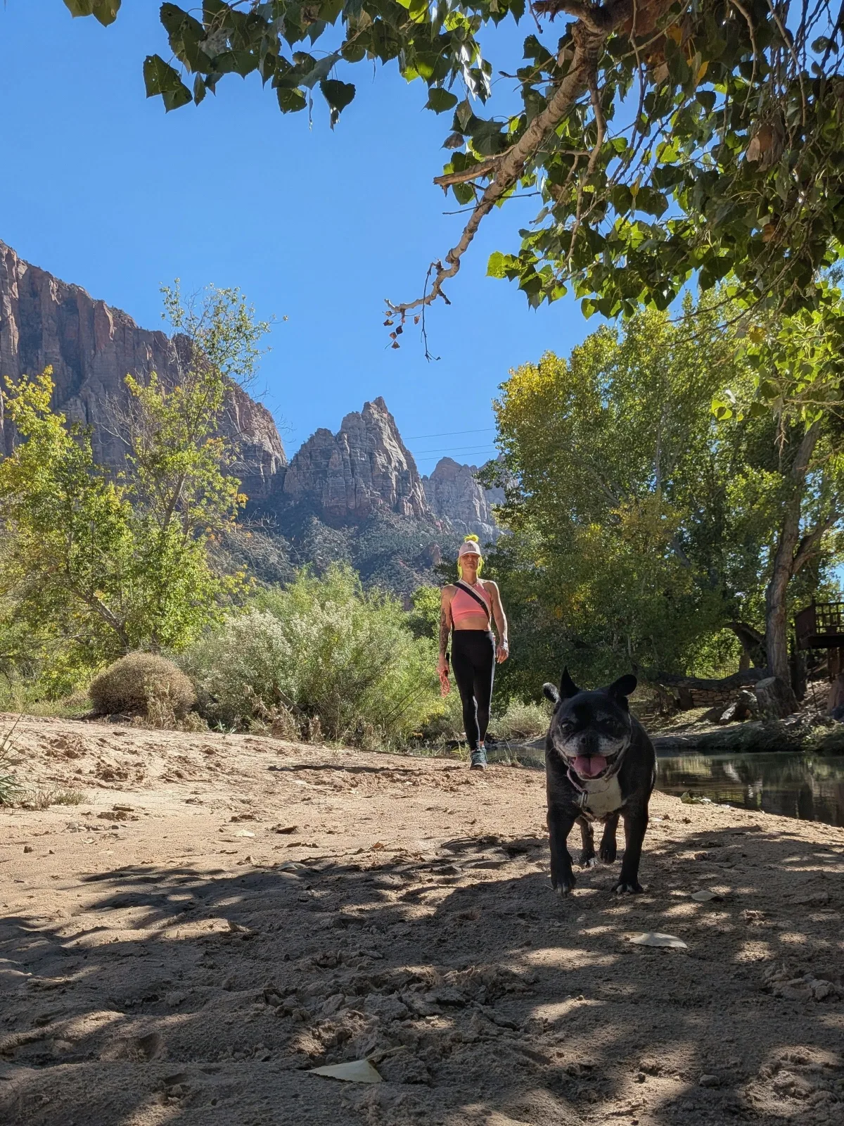 Tera, with neon yellow hair, hiking toward the camera behind Lucy, with red rock cliffs in the background
