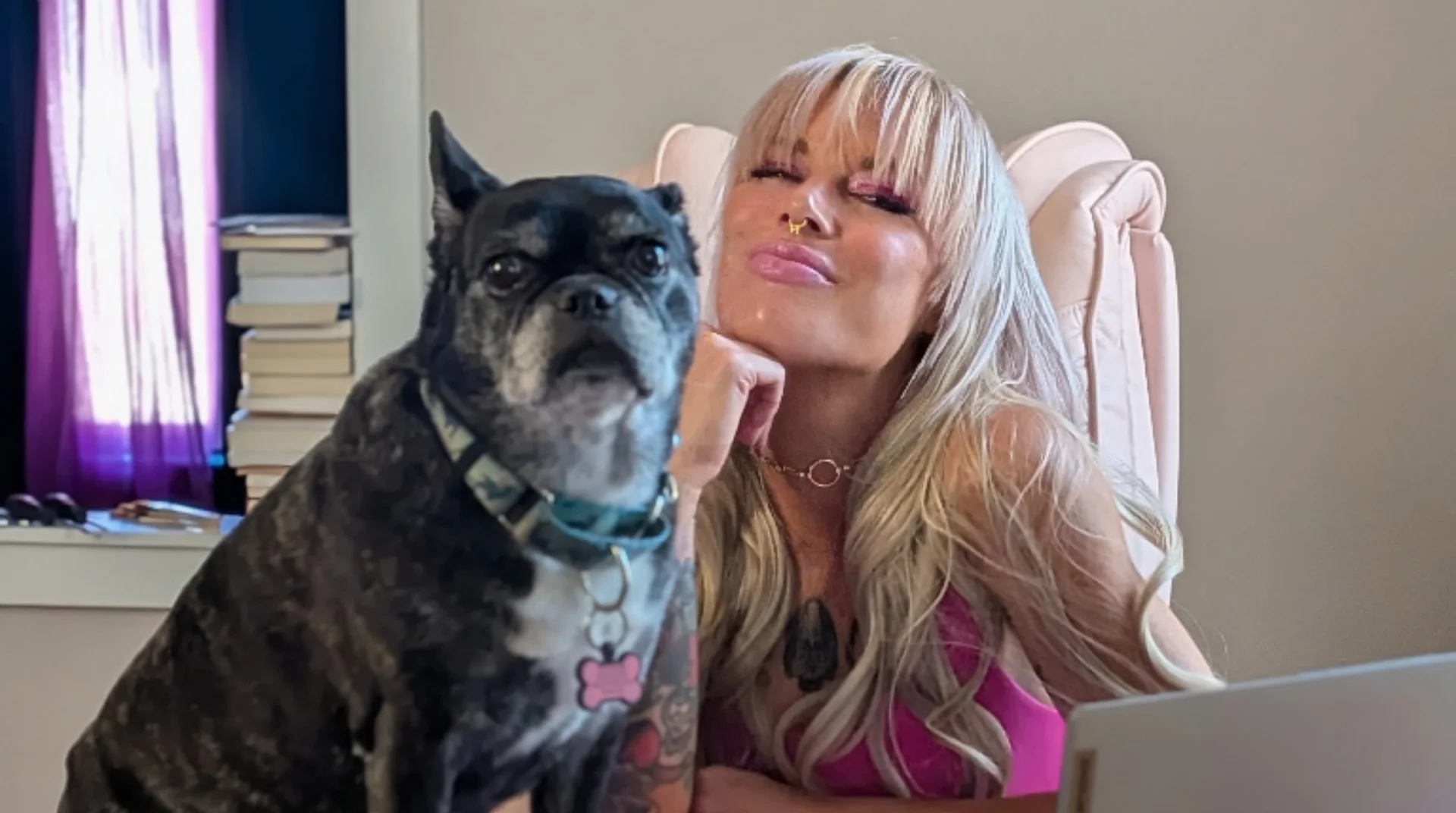 Tera Kidd at her desk in a pink chair, chin on her hand, with her dog Lucy sitting on the desk beside her