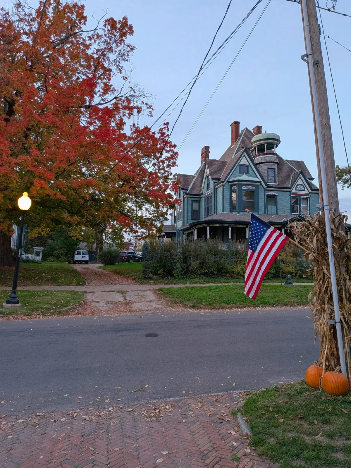 A blue Victorian with a copper-topped turret and wraparound porch behind a red maple